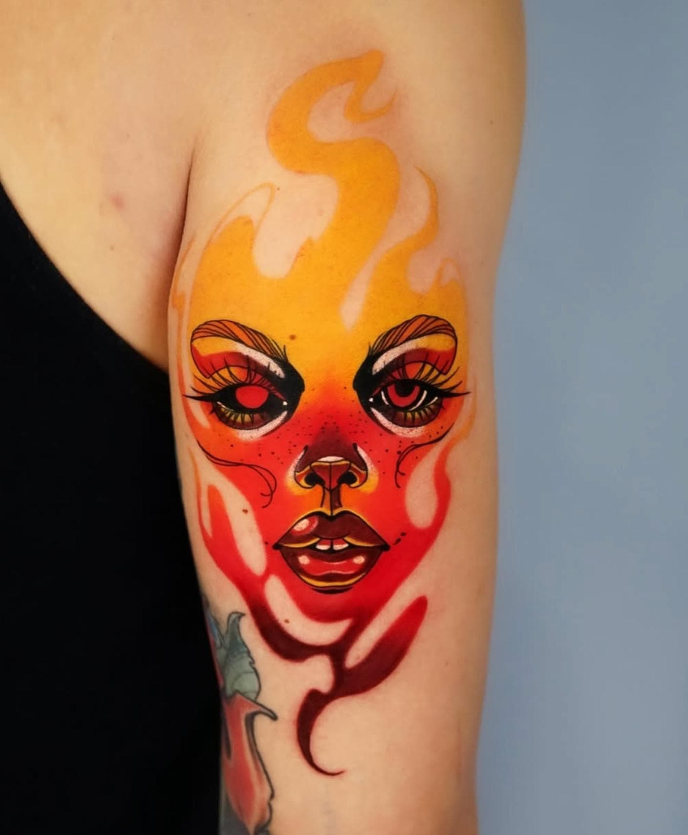 Colorful New School tattoo of a face with flames on the upper arm